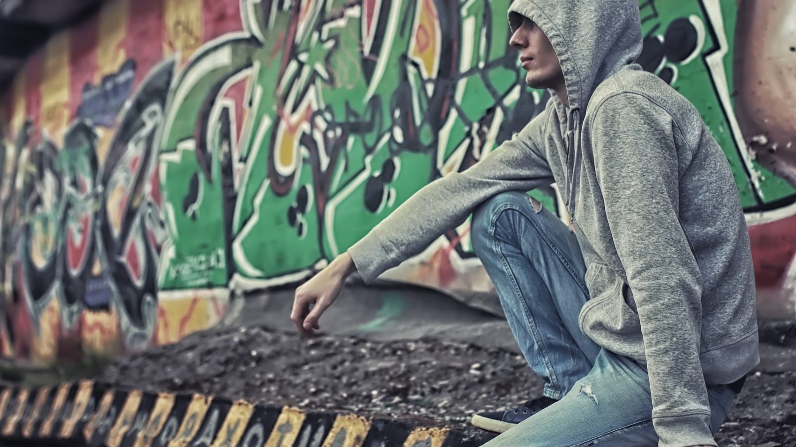 Ung kille sitter vid en grafittivägg.
