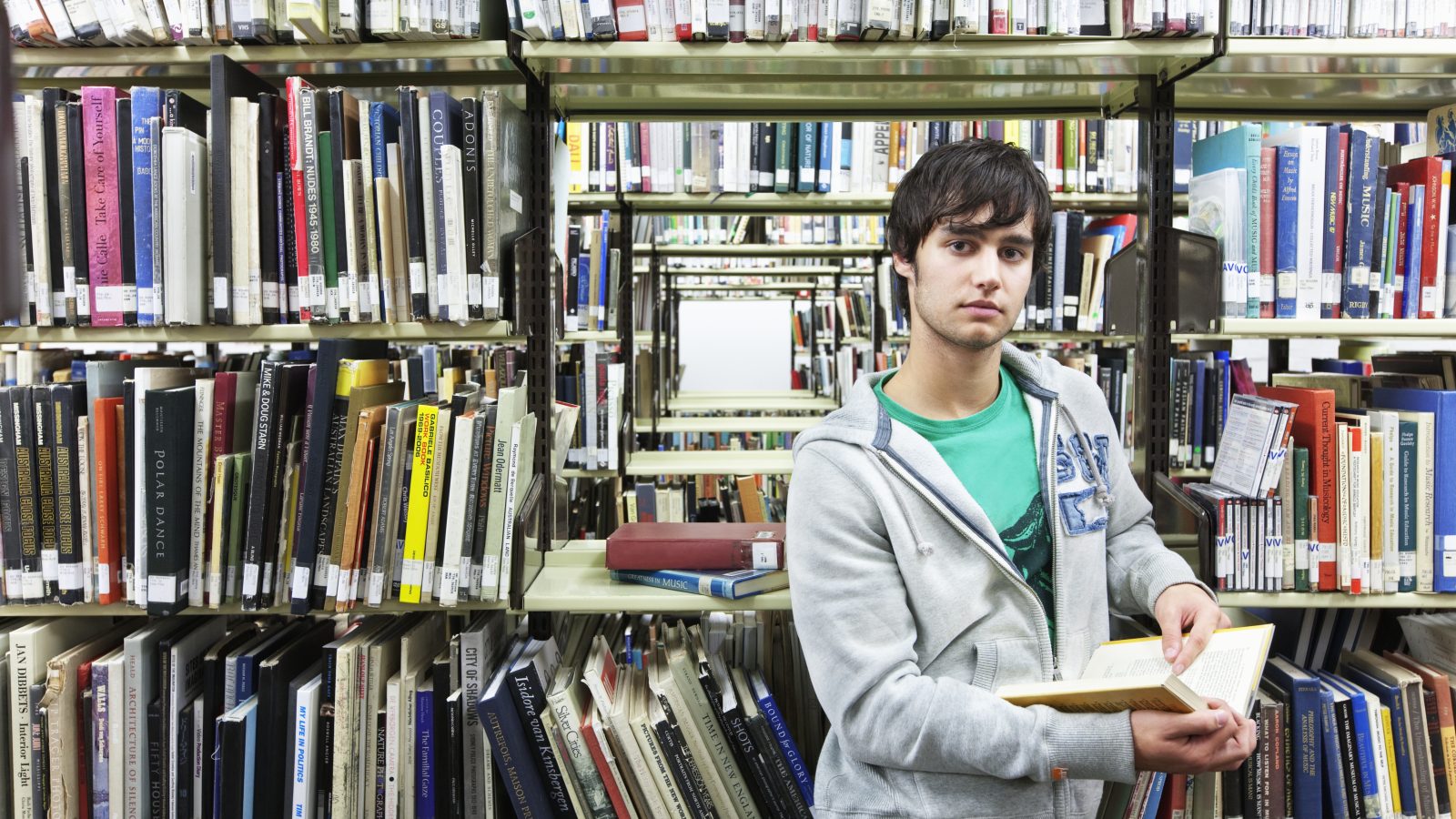 Ung man står och bläddrar i en bok i ett bibliotek