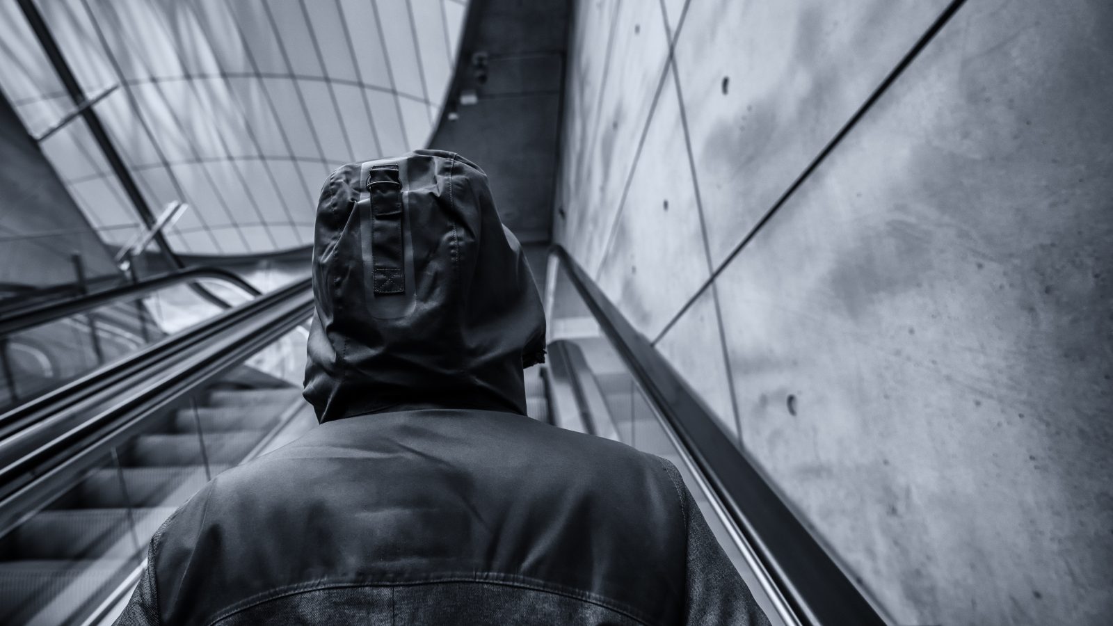 Svartvitt bild på person med hoodie som åker rulltrappa