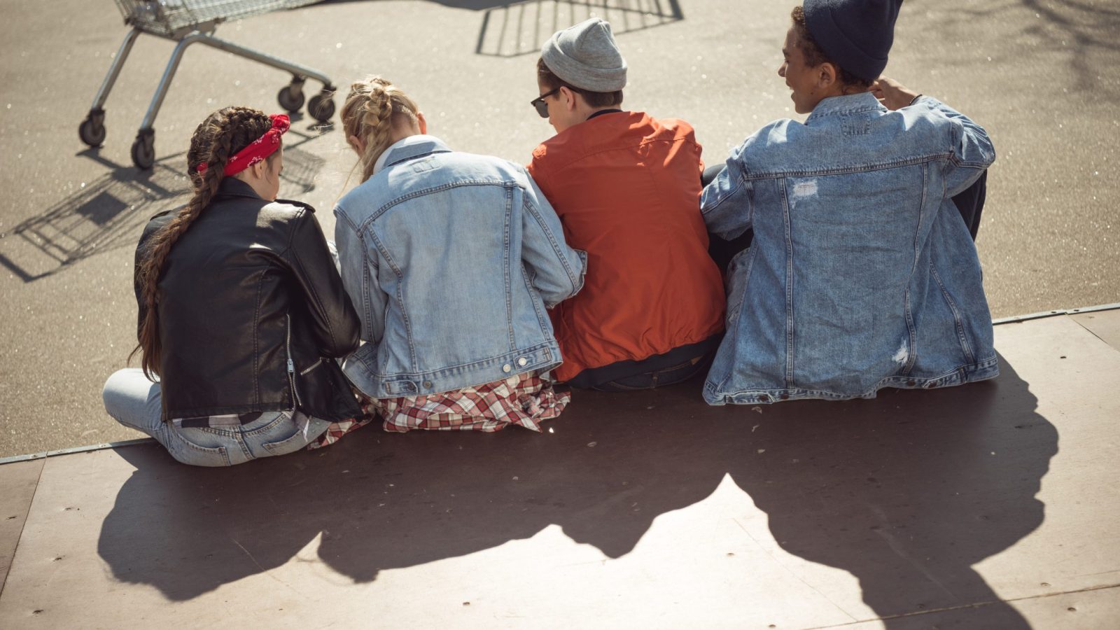 Bild tagen bakifrån på en grupp med tonåringar som sitter på trottoaren och pratar