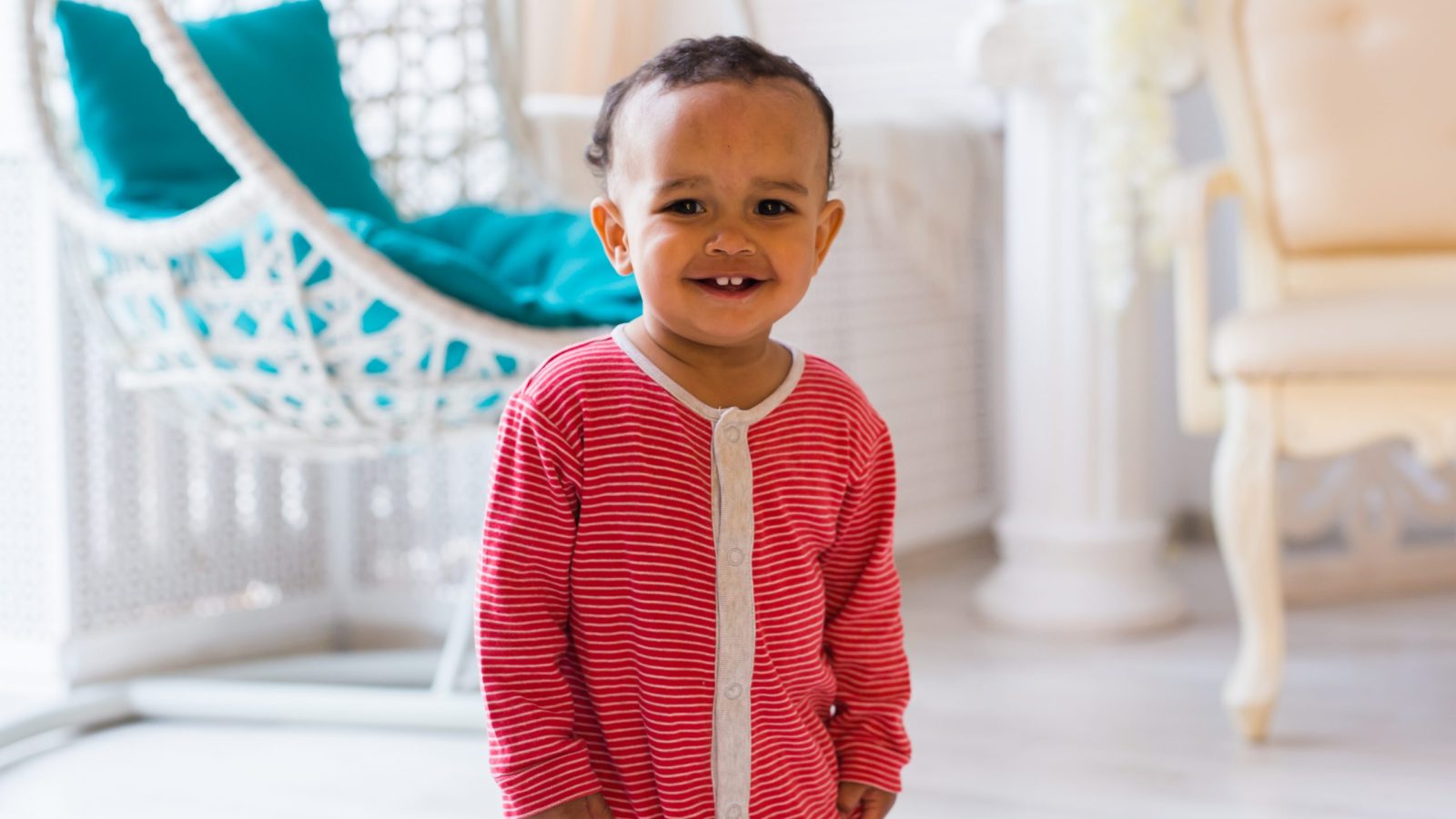 liten pojke runt ett år i röd pyjamas tittar in i kameran och skrattar