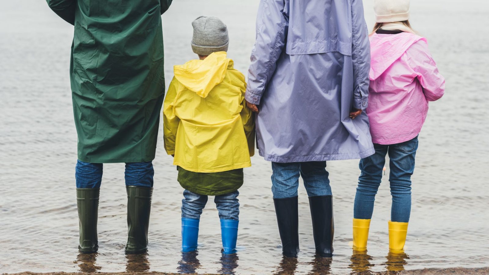 Två vuxna och två barn med regnkläder vid strandkanten