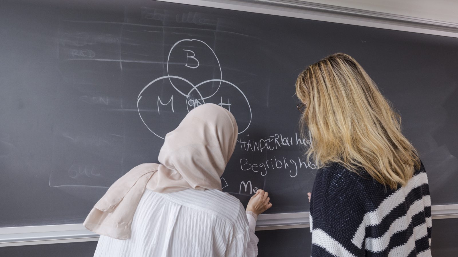 kvindelig elev og kvindelig underviser ved tavlen i klassevärelse