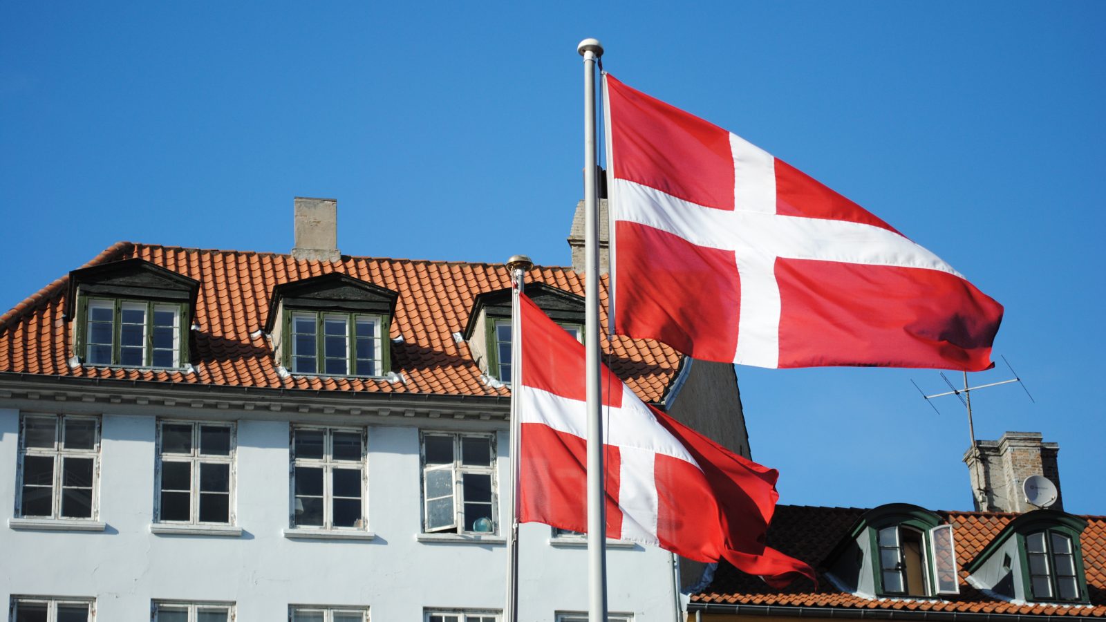 Två flaggstänger med danska flaggan i stadsmiljö