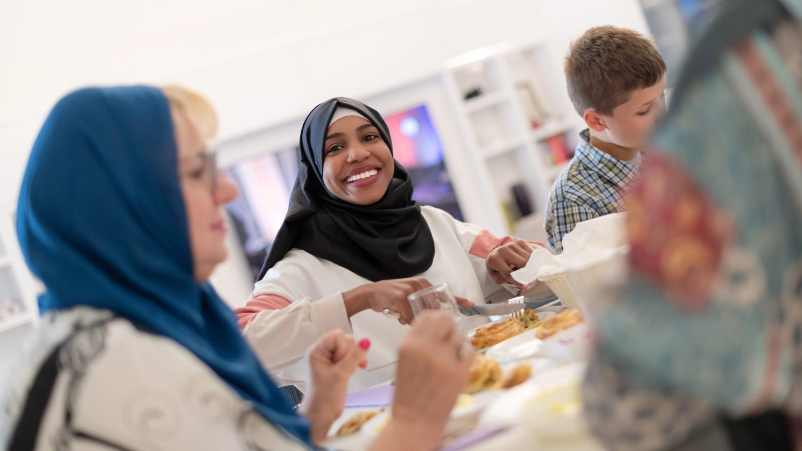 En grupp kvinnor i hijab äter middag tillsammans en lite pojke syns i bildens utkant
