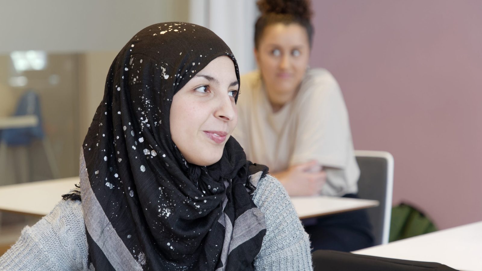 Kvinnlig elev som bör slöja i skolbänken i sitt klassrum under vuxenutbildning / svenska för invandrare