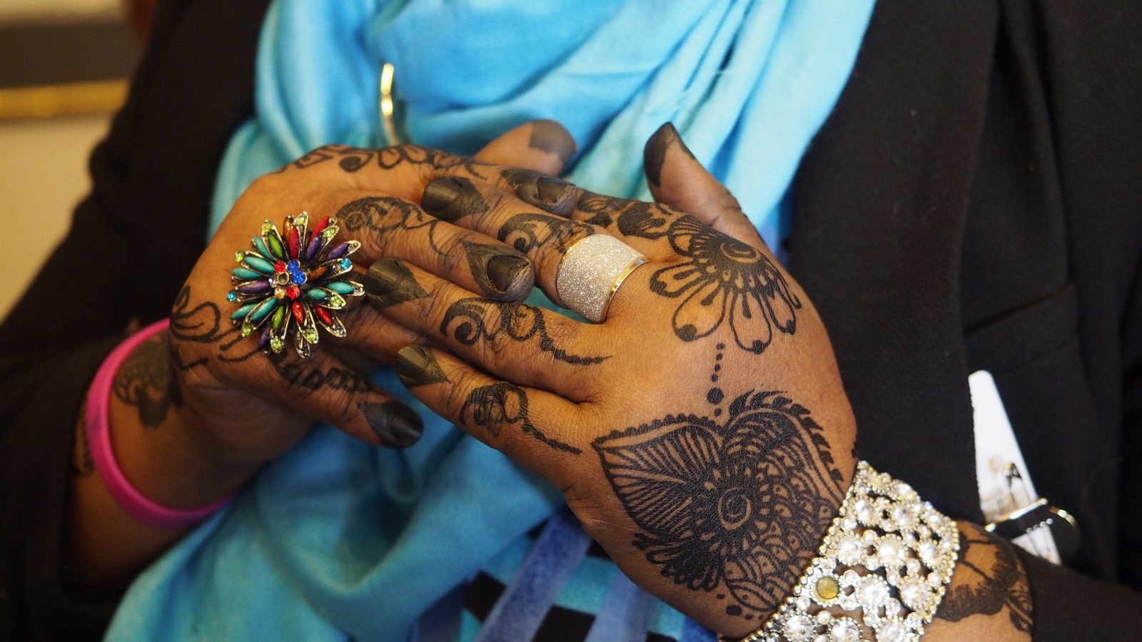 Närbild på händer med två stora ringar och hennatatuering