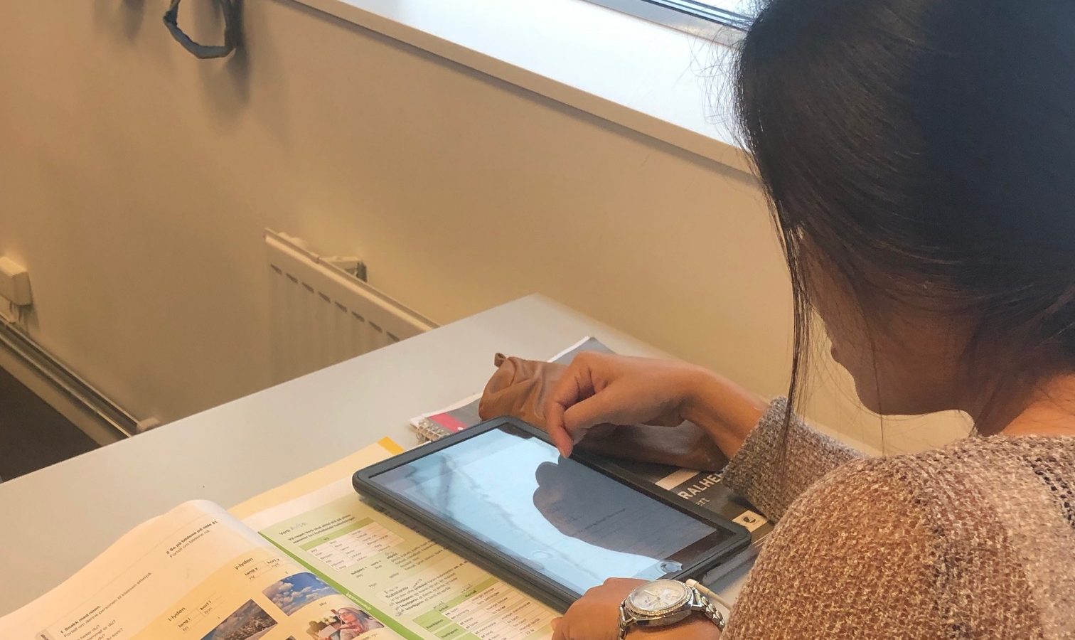 Kvinna med läsplatta och bok i skolbänk