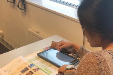 Kvinna med läsplatta och bok i skolbänk