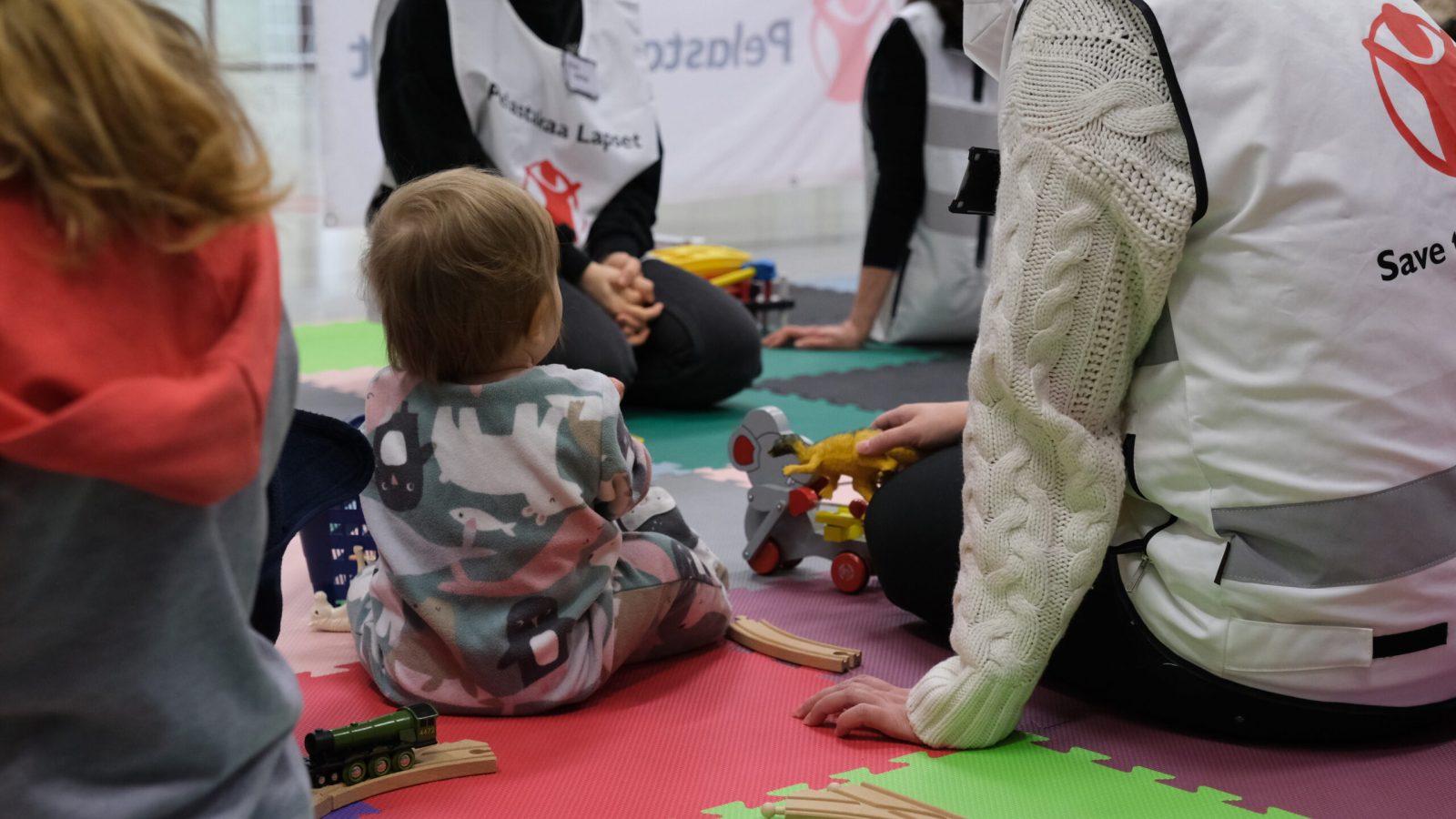 Ett litet barn som sitter på golvet, omringad av trygga vuxna.