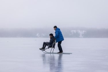 två pojkar på isen med en sparkstötting