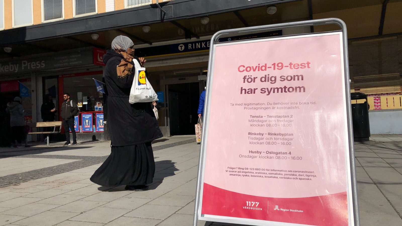 kvinna i hijab på Rinkebytorg paserar en skylt med Covid-information