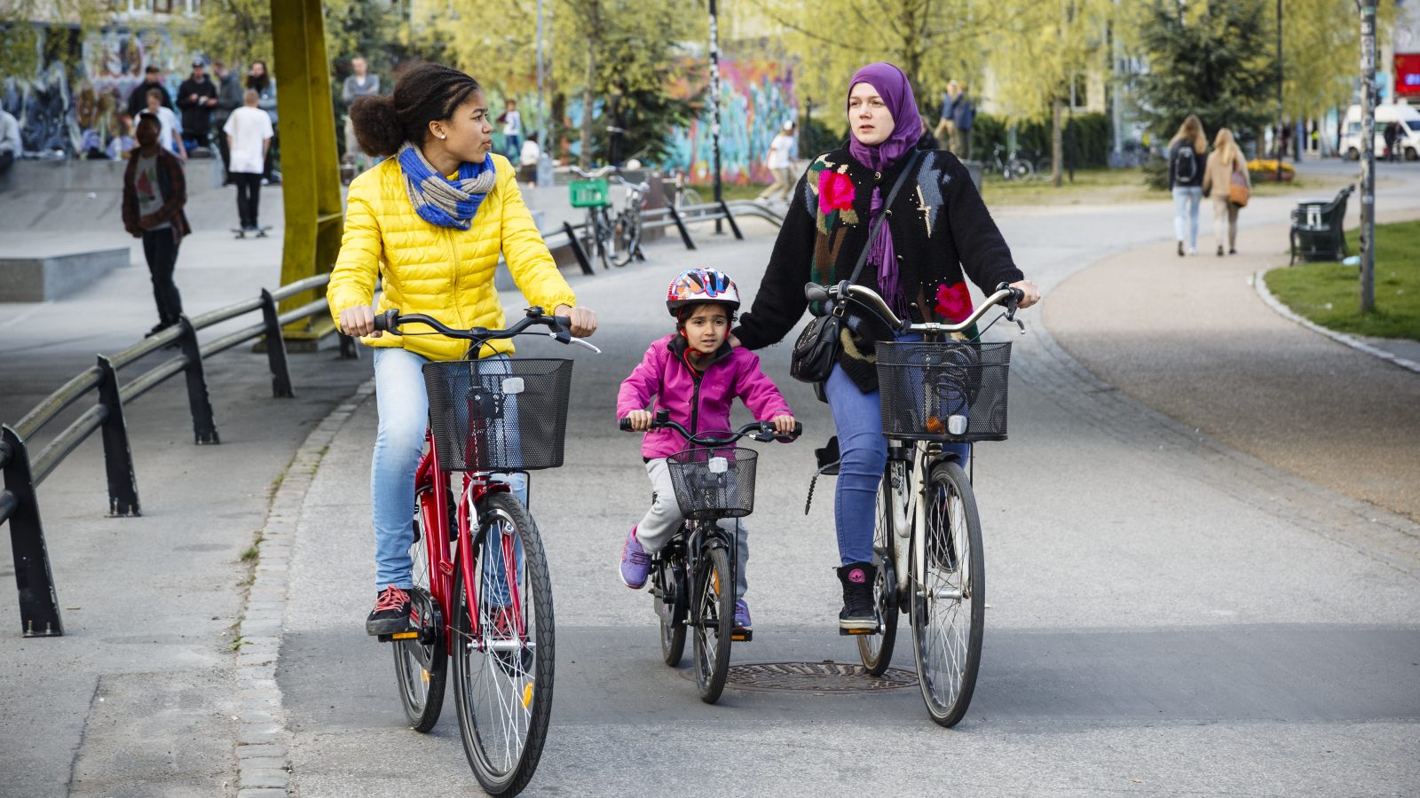 Kvinnor och barn cyklar i en park.