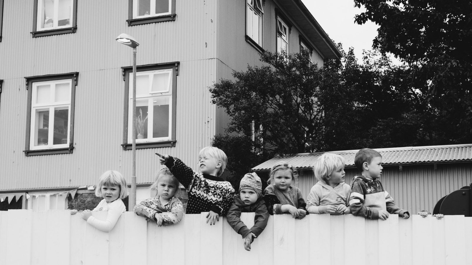 svart-vit bild av barn bakom ett plank, i bakgrunden syns ett hyreshus