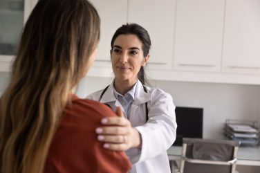 Positive satisfied young Latin doctor woman touching shoulder of patient with support, discussing good healthcare news, medical checkup result, successful therapy ending, smiling