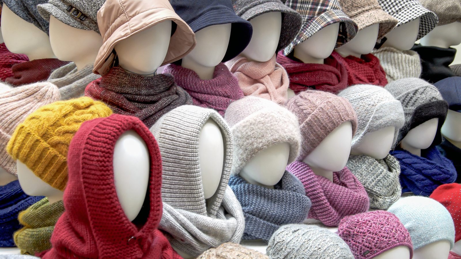 Showcase of trade tent with variety of women's hats for the autumn and winter seasons - knitted hats, scarves, hats. Small and medium-sized clothing business, product demonstration, seasonal sales.