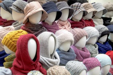 Showcase of trade tent with variety of women's hats for the autumn and winter seasons - knitted hats, scarves, hats. Small and medium-sized clothing business, product demonstration, seasonal sales.